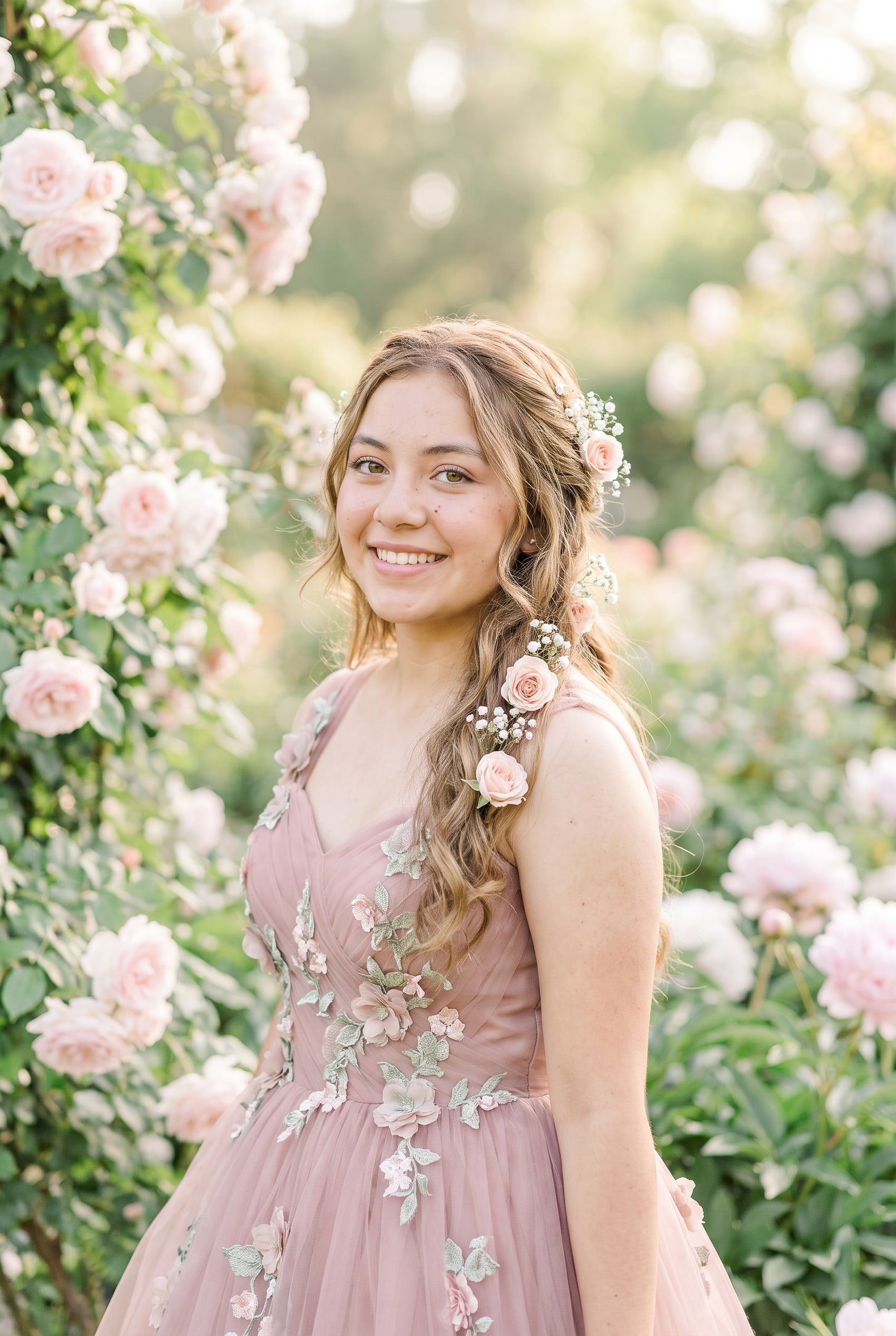 Camila con vestido rosa empolvado y flores en el cabello, en un jardín de rosas